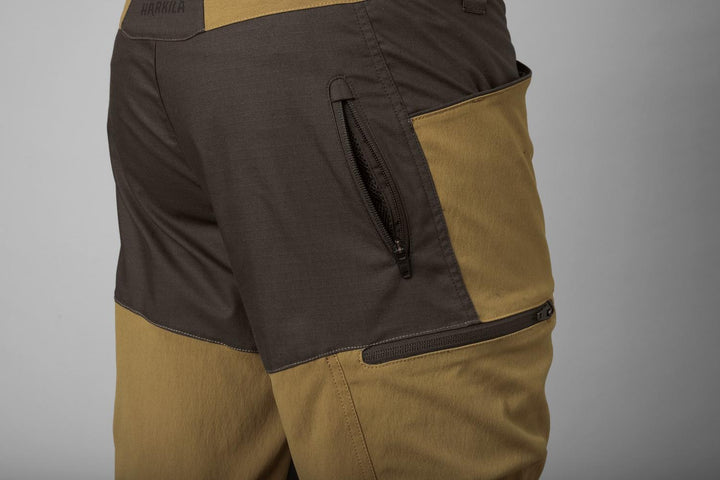 Three-quarter rear close-up of the Härkila Ragnar trouser hip, showing the zipped pocket set into the dark brown seat panel