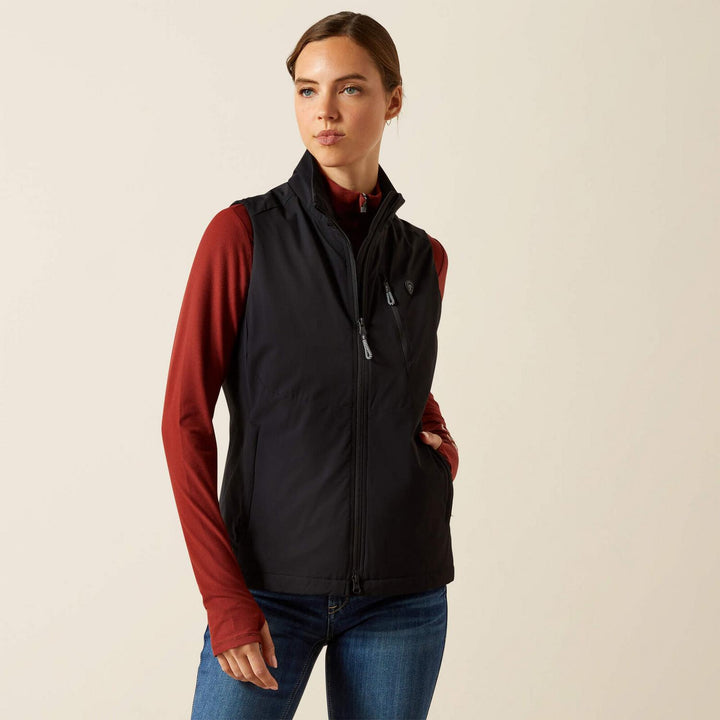 Woman wearing the Ariat Rion StretchShell insulated gilet in black over a red top, front view with the stand collar and zipped hand pockets