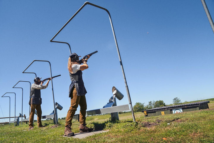 Lifestyle shot: wide view of a skeet range under blue sky, two clay shooters in Seeland shooting waistcoats at the stand