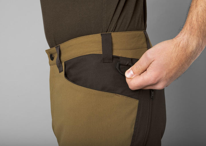Close-up of a hand pulling open the zipped side thigh pocket on the Härkila Ragnar trousers