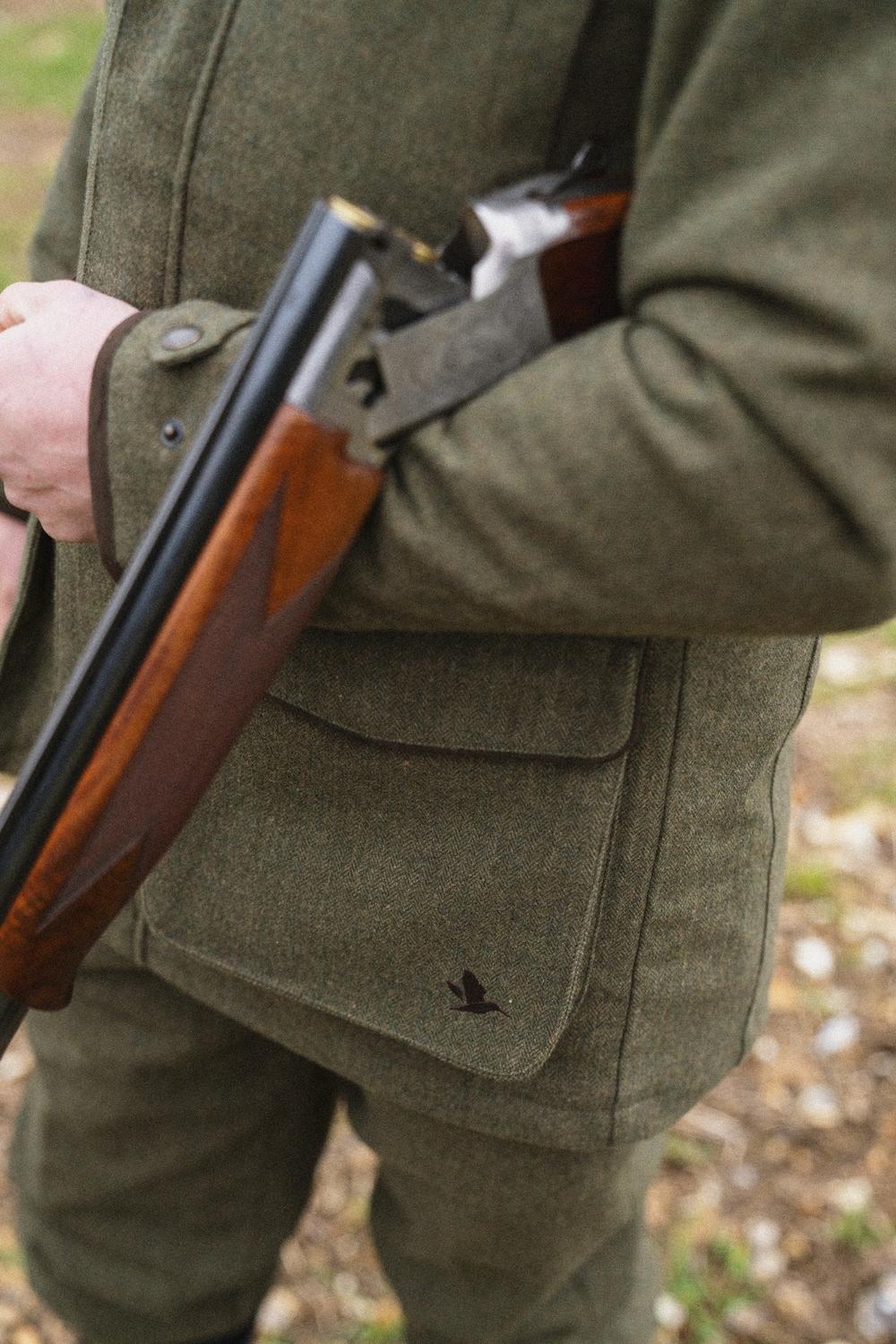 Close-up of a man breaking open a shotgun while wearing the Seeland Hillside jacket, showing the chest pocket with Seeland duck logo
