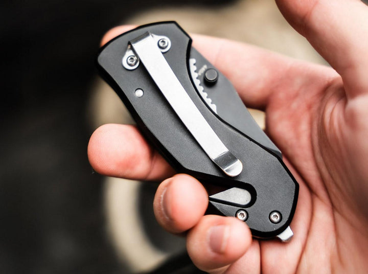 Hand holding the black Böker Magnum Black Rescue folding knife showing the pocket clip and glass breaker, lifestyle shot