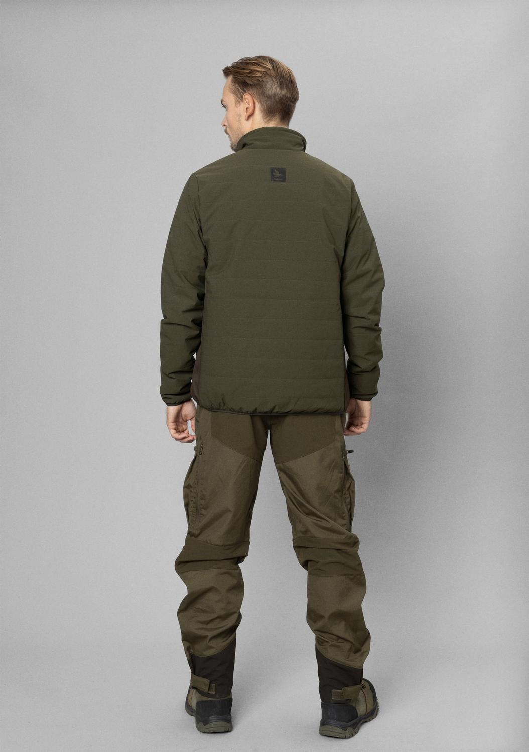 Model photographed from behind in the olive Celsius Heat jacket and matching green trousers against a grey studio wall.