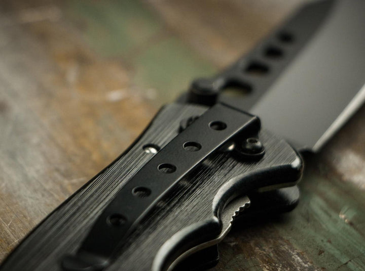 Close-up of Böker Magnum Special Forces black folding knife pocket clip and blade on a wooden surface