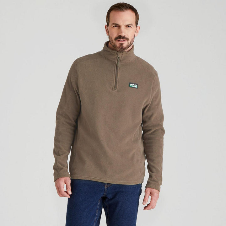 Male model wearing the Ridgeline Narvik fleece in taupe with blue jeans, front view cropped at the hip, showing the stand collar and chest zip.