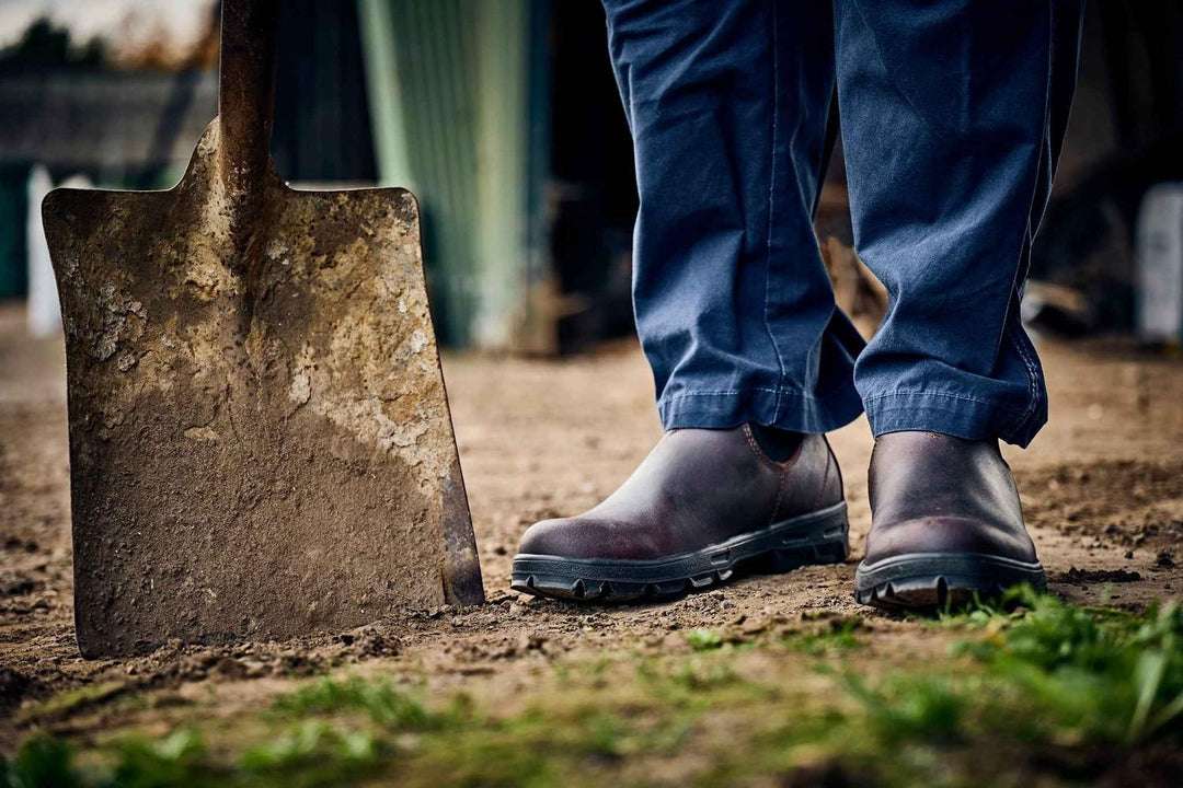 Lifestyle shot of Grubs Whirlwind brown dealer boots worn on a farm yard beside a muddy spade