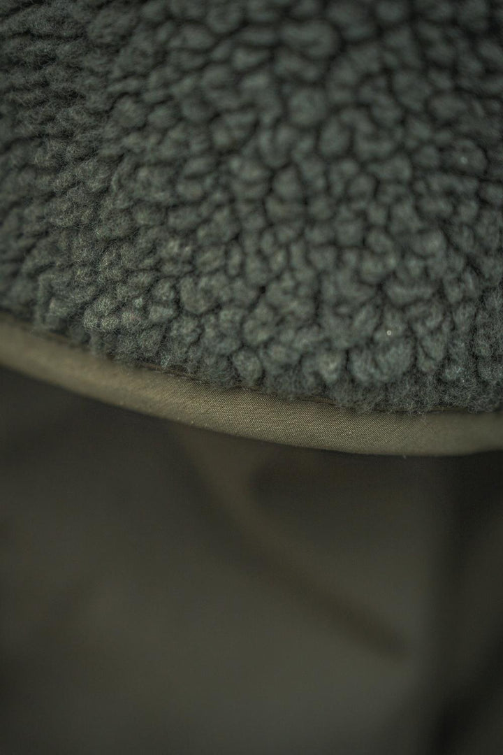 Macro of the fabric junction where the deep curly pile fleece meets the smooth shell panel along a bound seam.