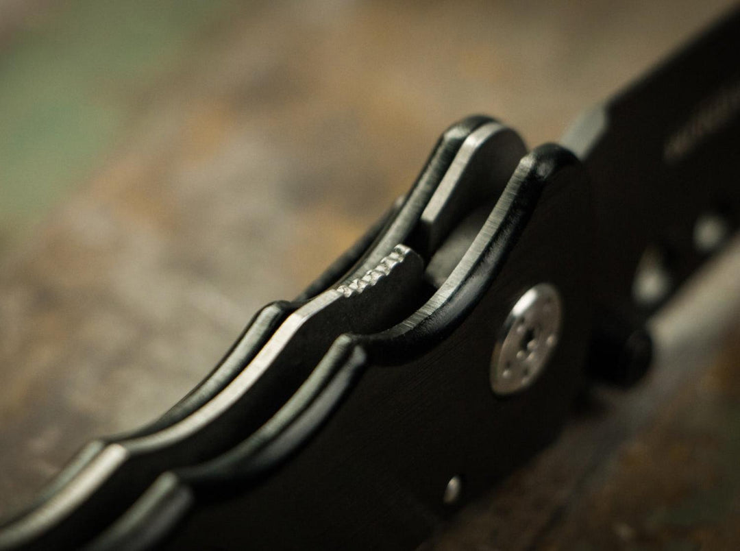 Close-up of Böker Magnum Special Forces black folding knife handle and thumb stud on a wooden surface