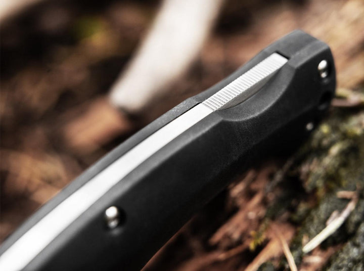 Close-up of the black handle and satin blade of the Böker Magnum Echidna folding knife on forest ground, lifestyle shot
