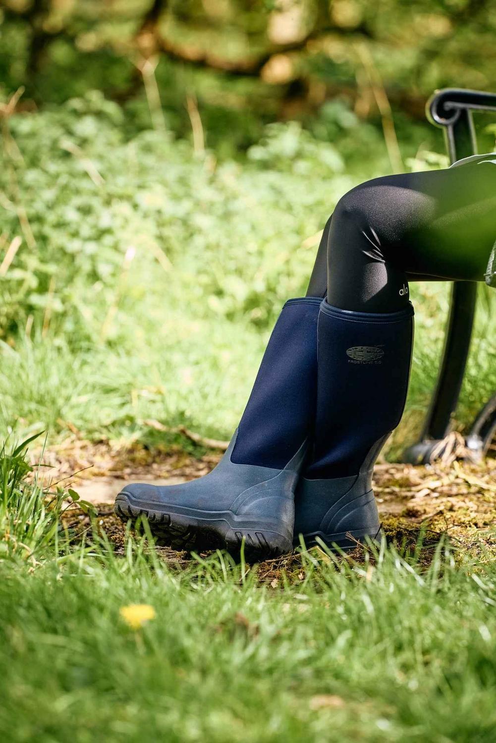 Navy Grubs Frostline 5.0 insulated wellington boots worn by a seated person on a grassy field