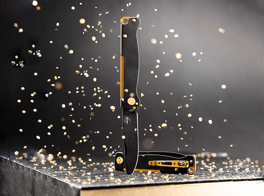 Two Böker Plus Atlas knives with black handles and brass accents standing among golden sparks, lifestyle shot