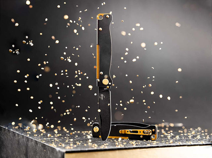 Two Böker Plus Atlas knives with black handles and brass accents standing among golden sparks, lifestyle shot