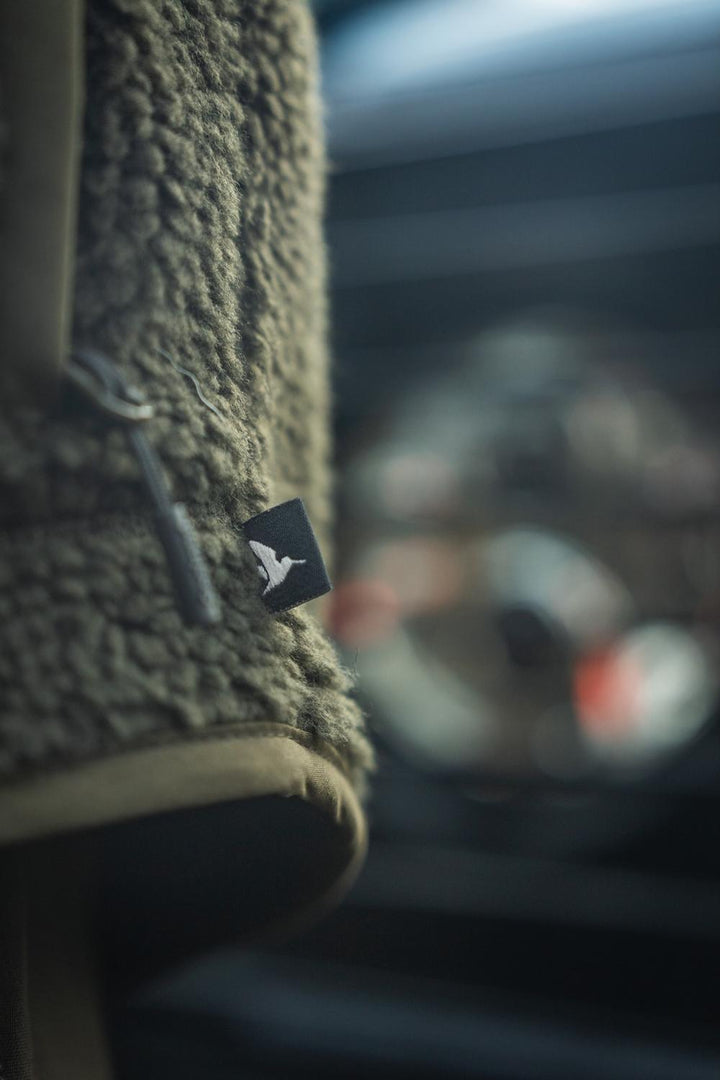 Lifestyle detail of the hem and hand pocket with the Seeland pintail tag on the zip, blurred vehicle interior behind.