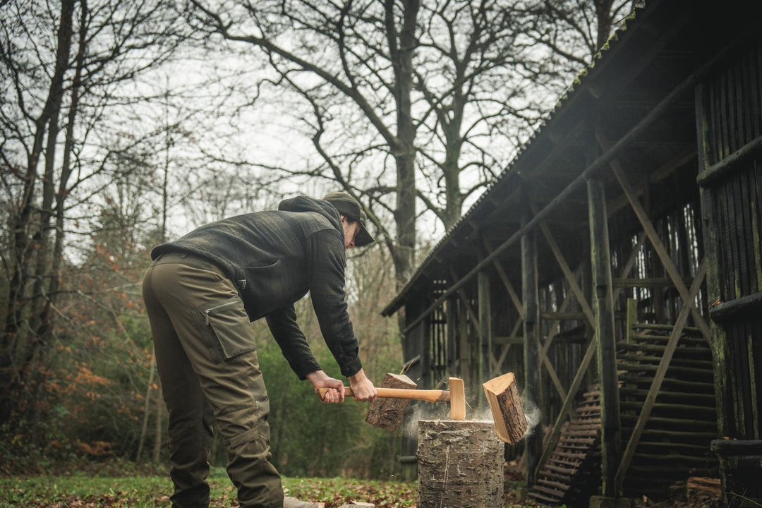 Lifestyle shot: a man in the Seeland Canada Yukon jacket splits logs on a chopping block beside a wooden barn
