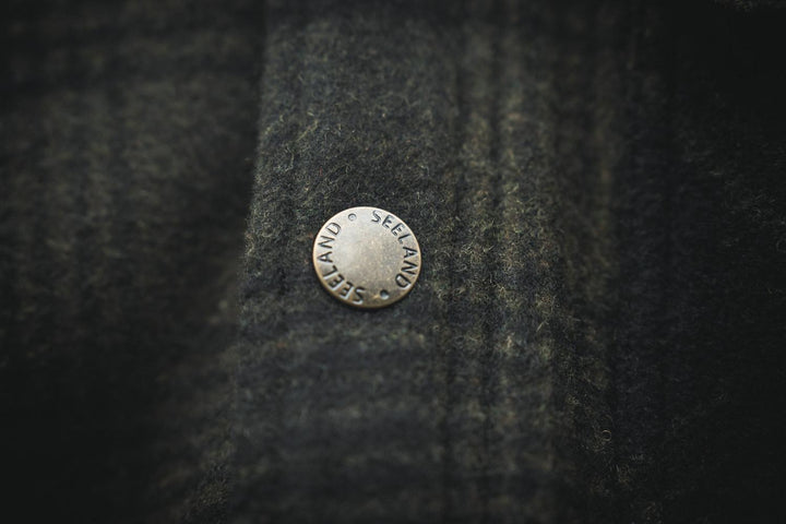 Close-up of a metal SEELAND-embossed press stud on the check wool of the Canada Yukon jacket