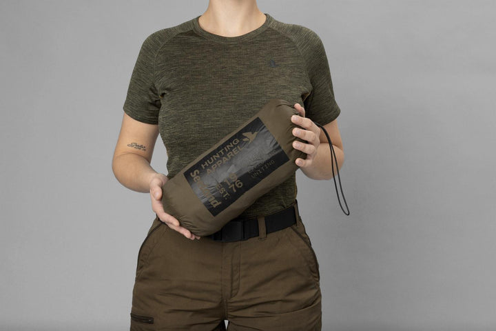 Model holding the jacket packed down into its olive Seeland stuff sack, printed Hunting Apparel Est. 1976 panel and a black elastic drawcord.