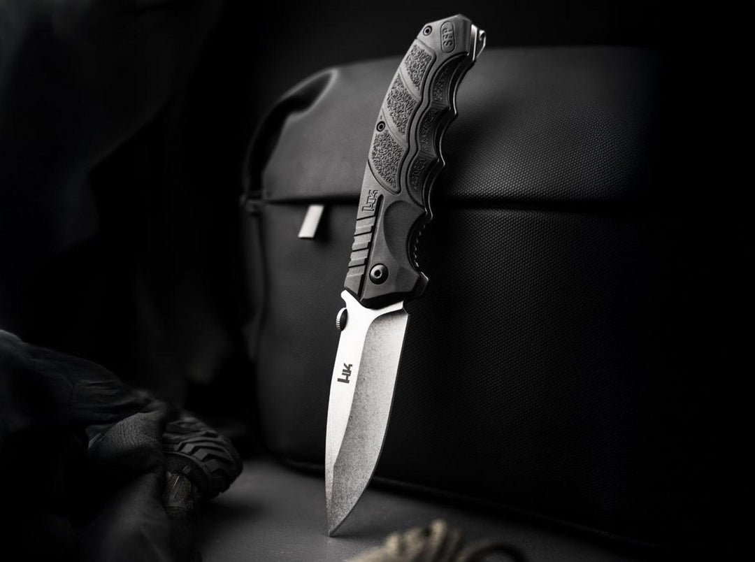 Böker SFP Tactical folding knife standing open against a black bag in a dark lifestyle shot