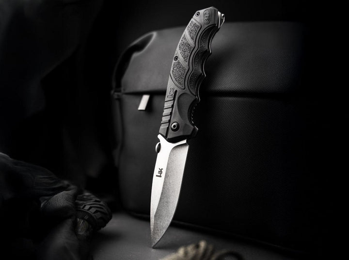 Böker SFP Tactical folding knife standing open against a black bag in a dark lifestyle shot