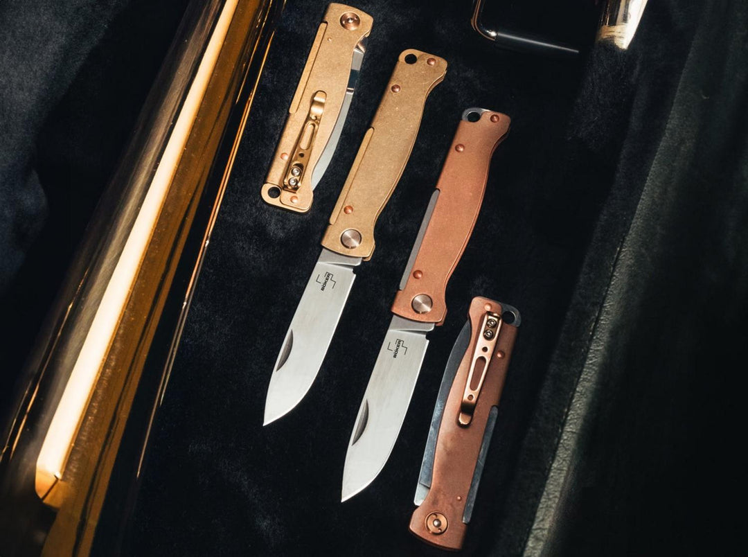 Böker Plus Atlas knives in copper, brass and other finishes laid out on black velvet in a presentation case, lifestyle shot
