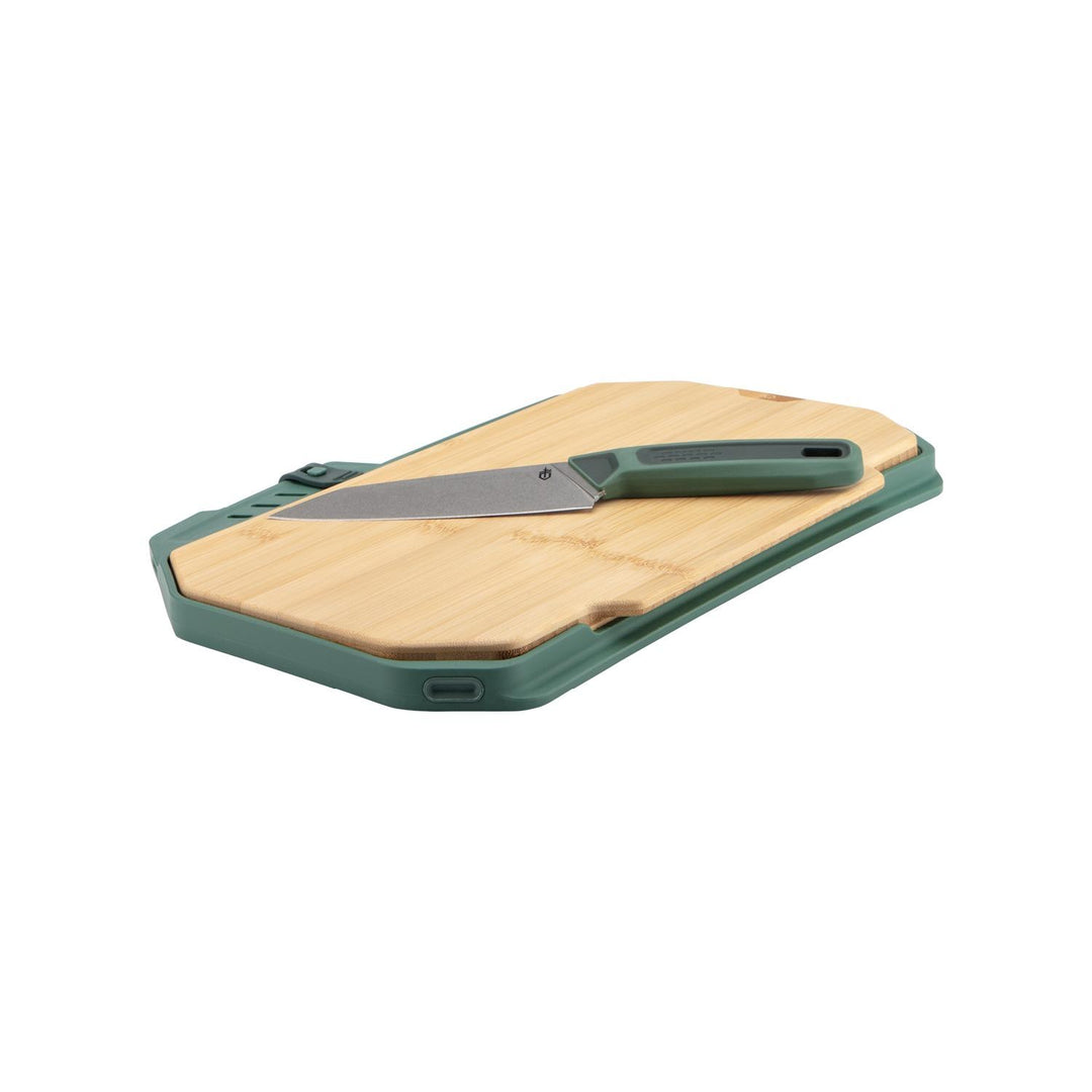 Gerber ComplEAT Slim cutting board set, bamboo board seated in a green plastic tray with the folding knife stowed alongside, three-quarter view