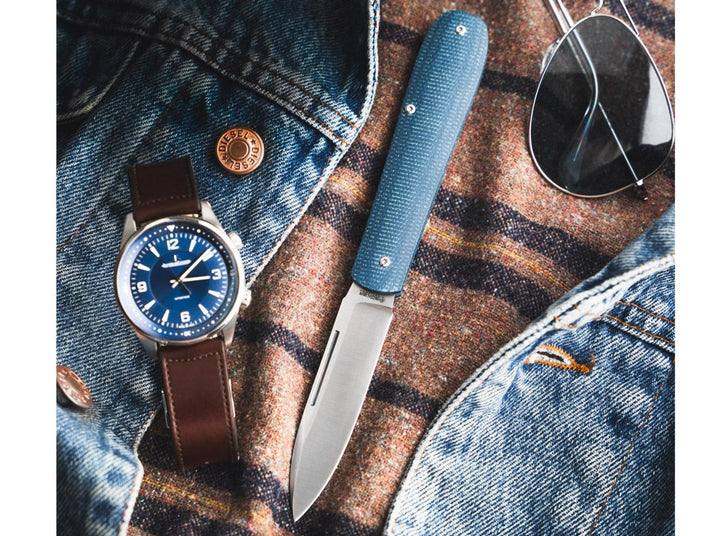 Blue Böker Coffin pocket knife lying on a denim jacket beside a wristwatch and sunglasses, lifestyle shot