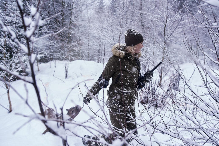 Lifestyle: woman carrying a rifle wading through deep snow in a snowy woodland clearing