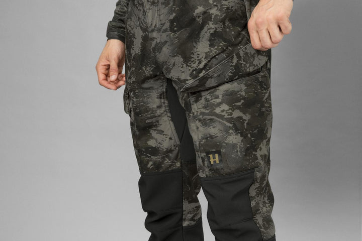 Model photographed front-on from the waist down, showing the cut through the thigh and the Harkila H logo on the knee panel