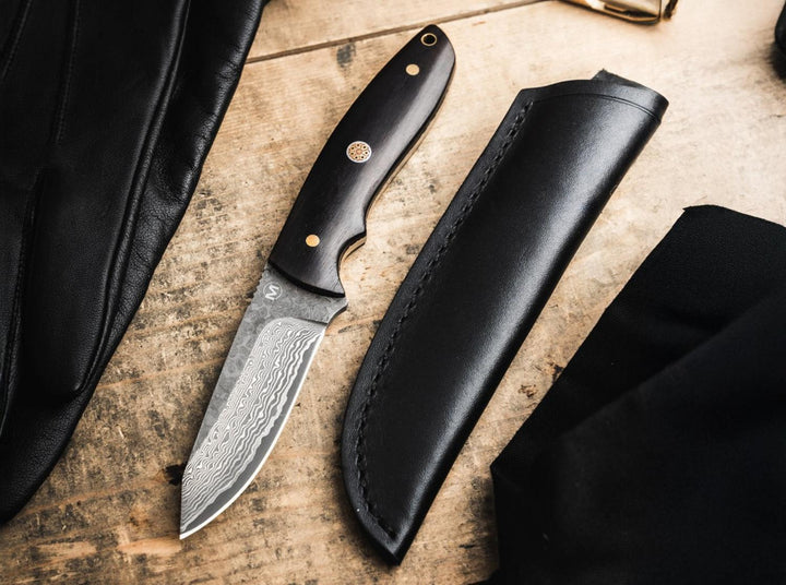 Böker Magnum Vernery Damascus knife with black leather sheath on a worn wooden surface, lifestyle shot