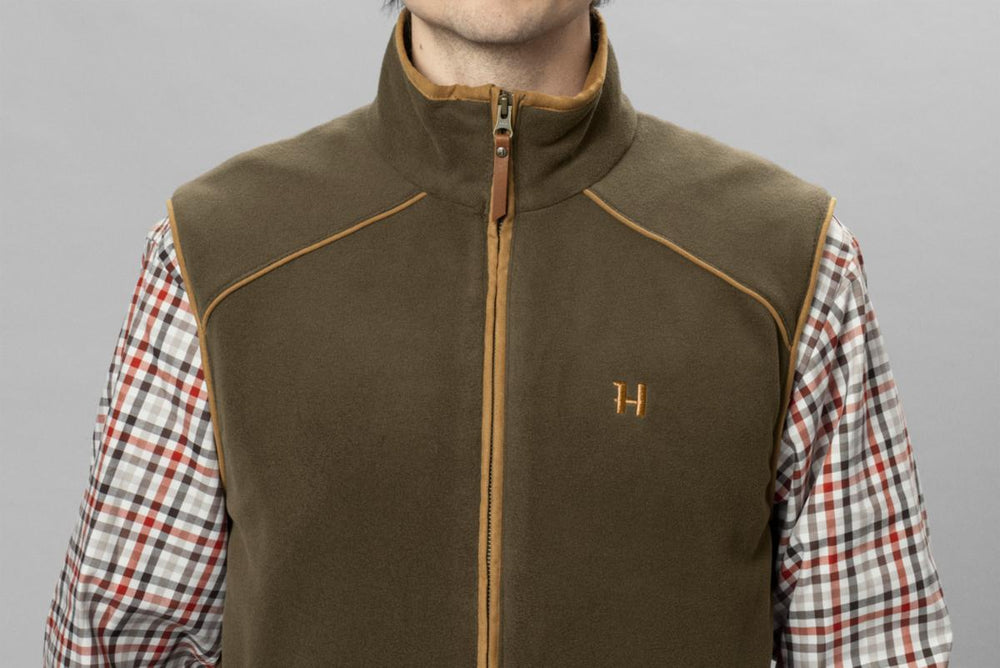 Close-up front view of a model in the olive Härkila Sandhem 200 waistcoat over a red and white check shirt