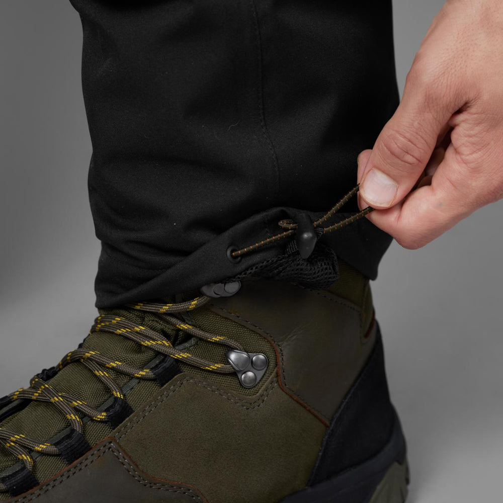 Detail of a hand pulling the hem drawcord tight over an olive leather walking boot.